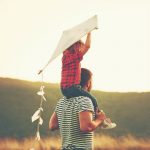 man with son on shoulders flying kite